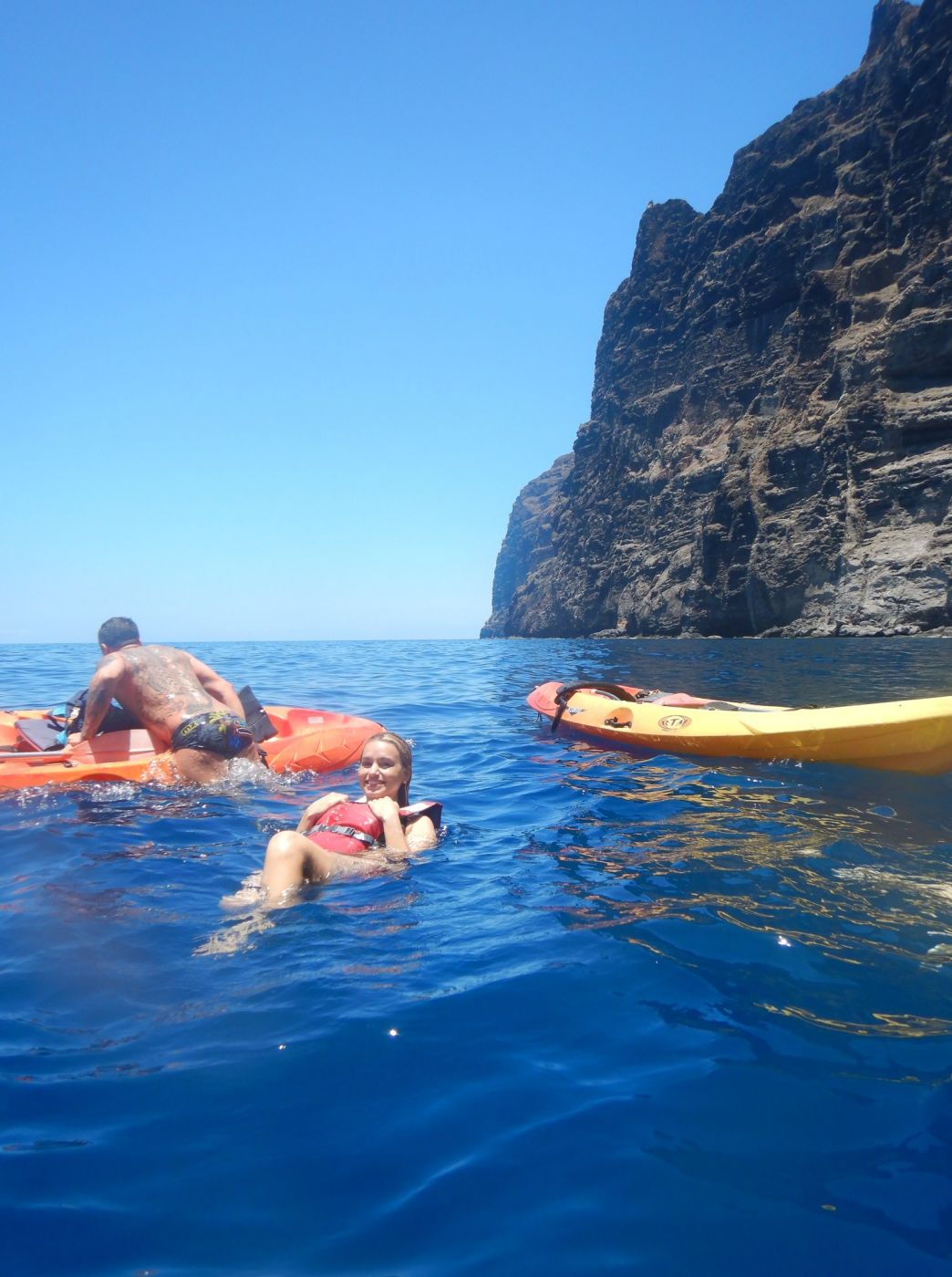 People swimming and kayaking near the cliffs.