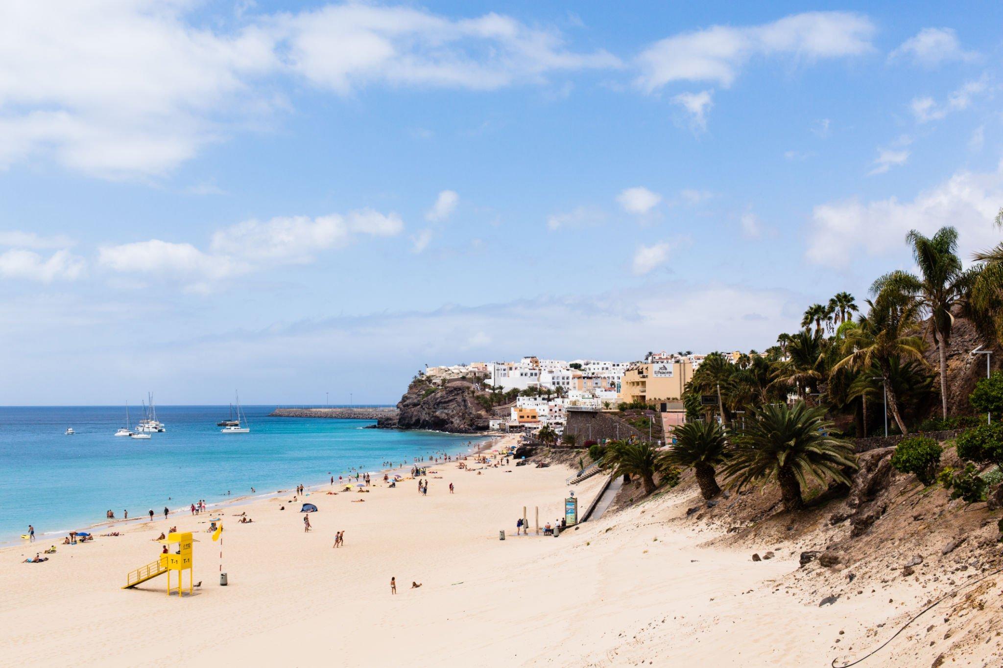 Morro Jable beach with palm trees and the town on the cliff