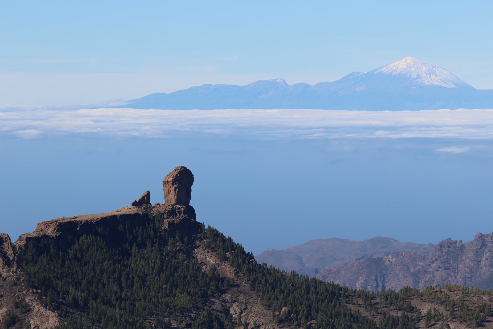 Monolito basáltico del Roque Nublo alzándose sobre las cumbres de Gran Canaria con el Teide al fondo